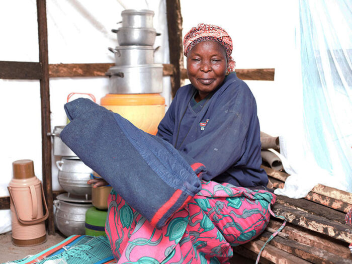 Supono from Nigeria sits in a Bama shelter holding a blanket and other ShelterBox aid