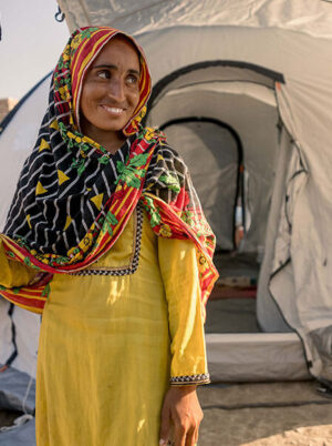 Woman in yellow smiles outside emergency relief tent in Pakistan after flooding