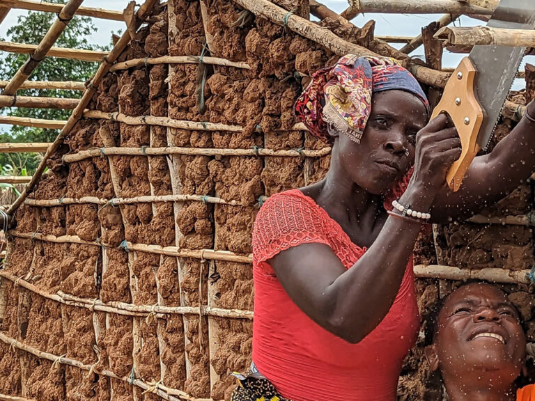 Lady sawing wood on the roof of a new structure supported by others