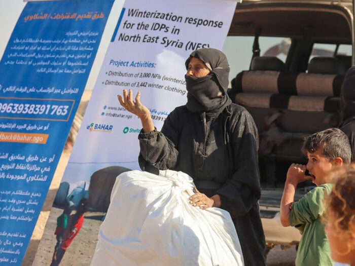 Woman and child with a bag of aid i front of a banner in Syria