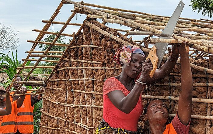 Woman sawing wood on the roof of a new shelter in Mozambique