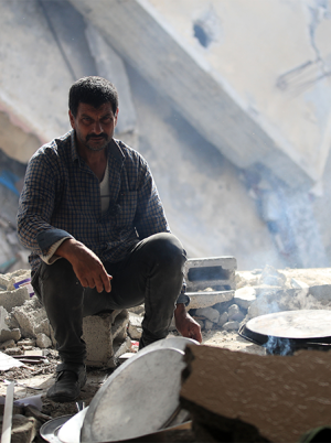 Man crouching in rubble of destroyed buildings Gaza