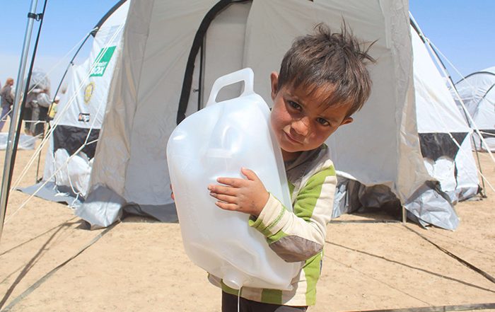 Boy in front of tent holding water carrier