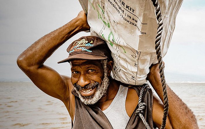 Man carrying shelter kit next to sea in Vanuatu